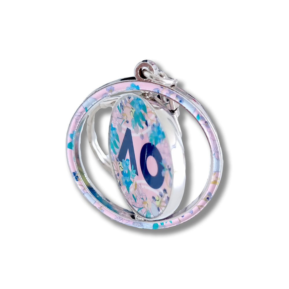 Close up: AO Logo Flower Keyring featuring a floral print design, the iconic AO logo, and a spinning disc silhouette with a split keyring attachment and silver chain.